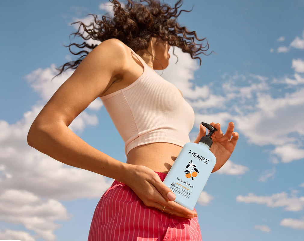 Woman holding a Hempz Triple Moisture lotion against a blue sky